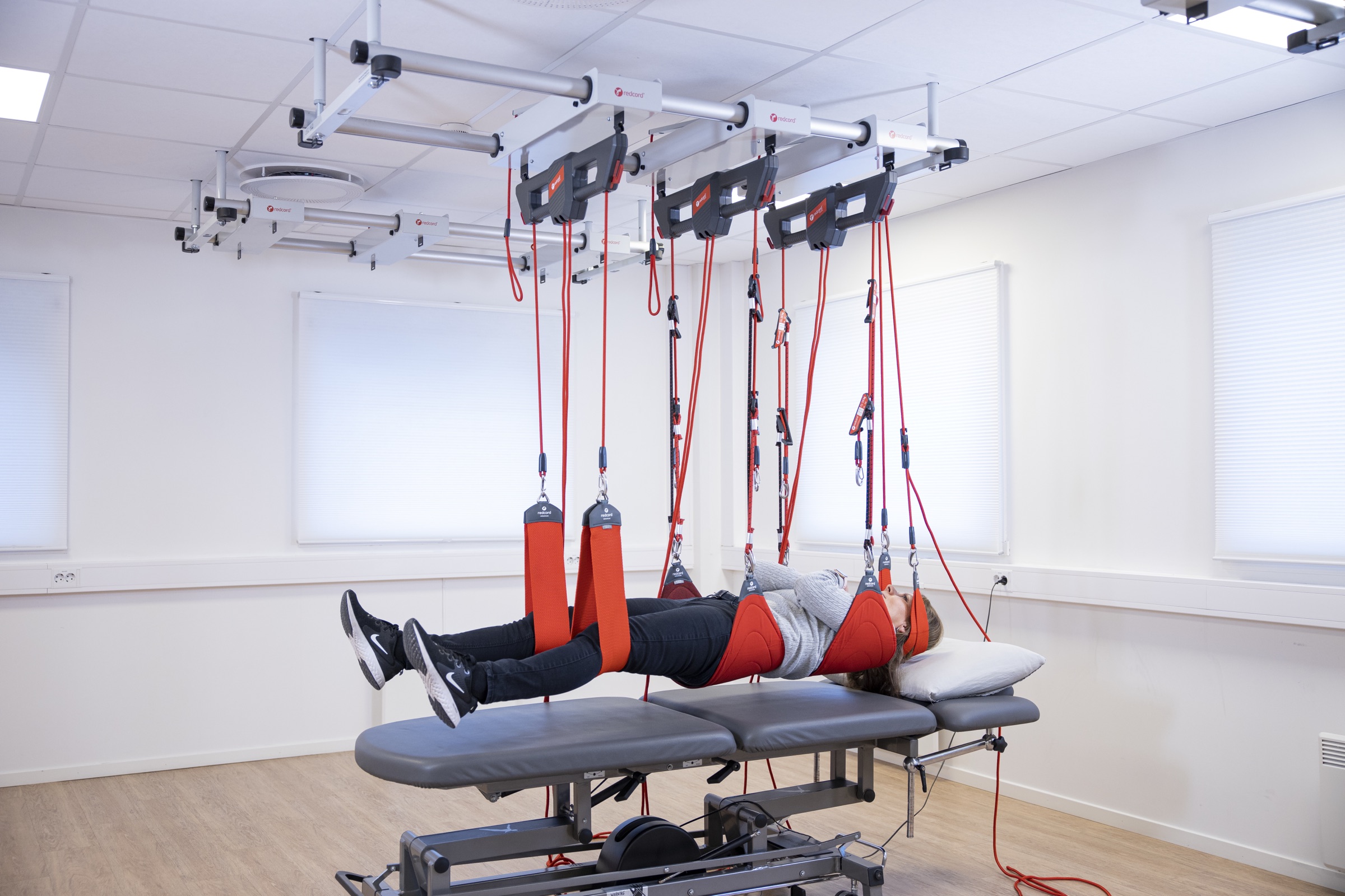A person lying on a treatment table, fully supported in red Redcord slings in a bright clinic
